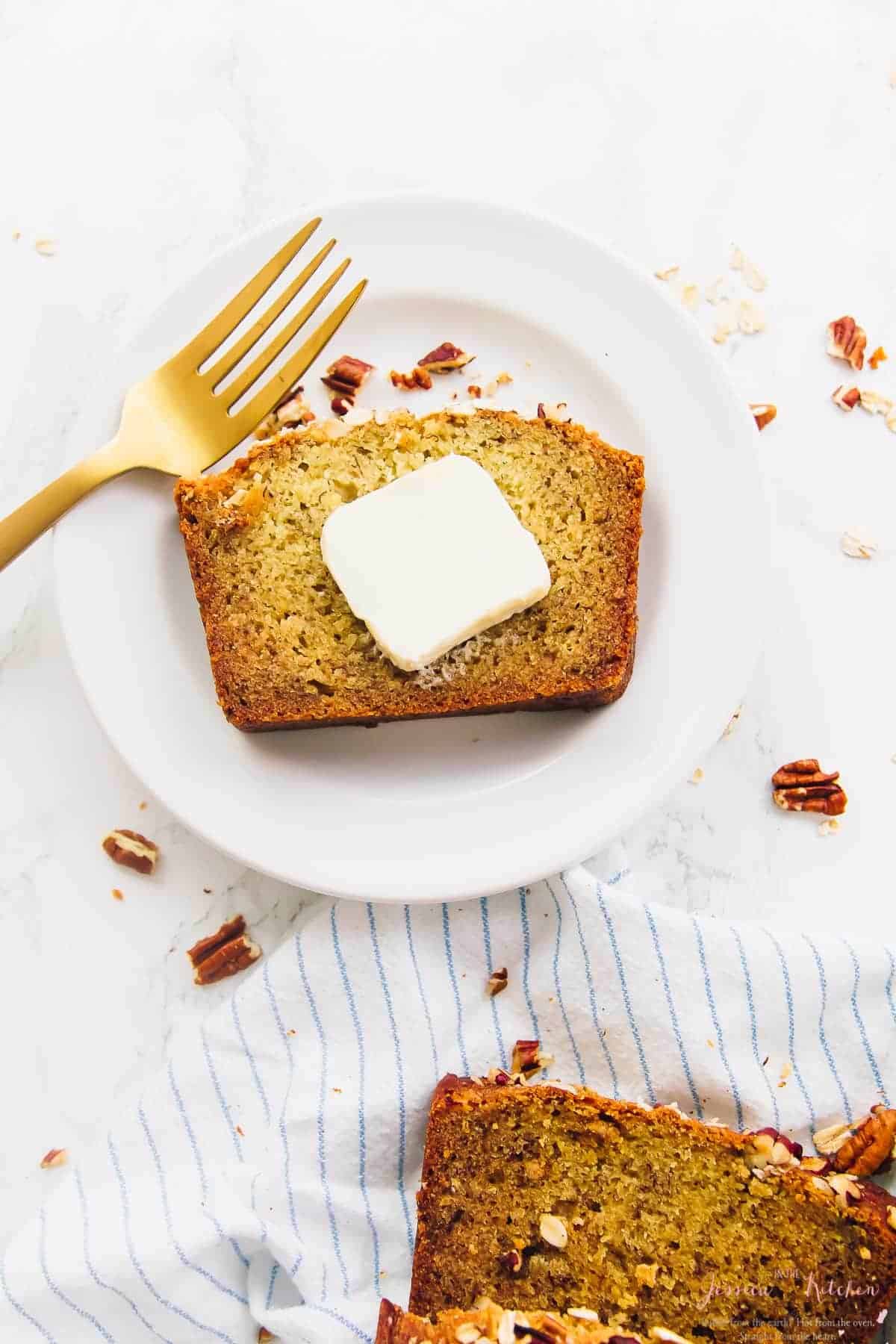 Overhead view of gluten-free vegan banana bread slice on plate with pat of butter
