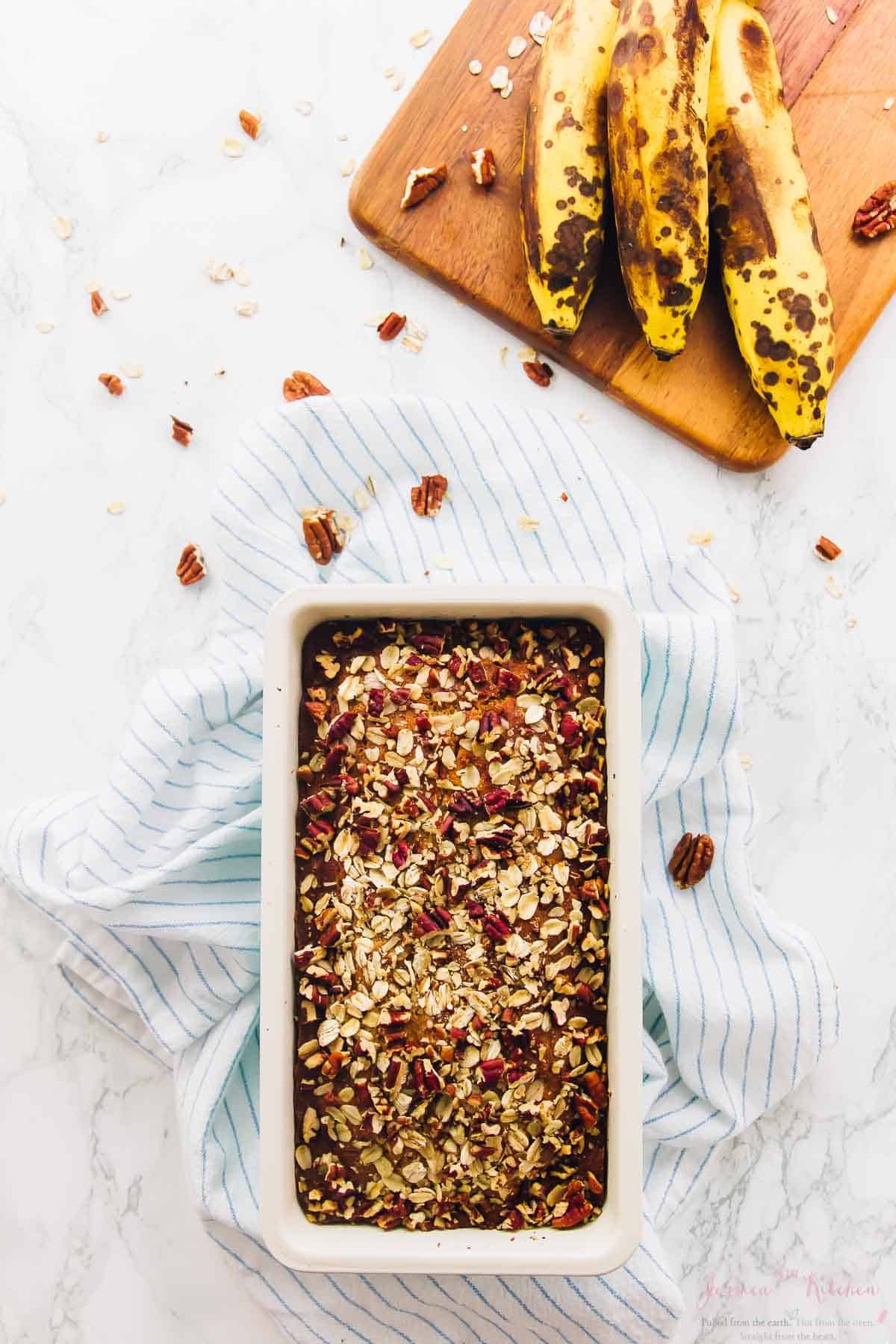 Overhead view of gluten-free vegan banana bread in loaf pan with bananas on cutting board in background