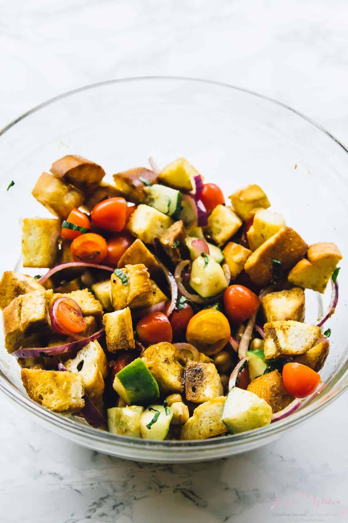 Cubed bread and diced vegetables in a glass bowl. 