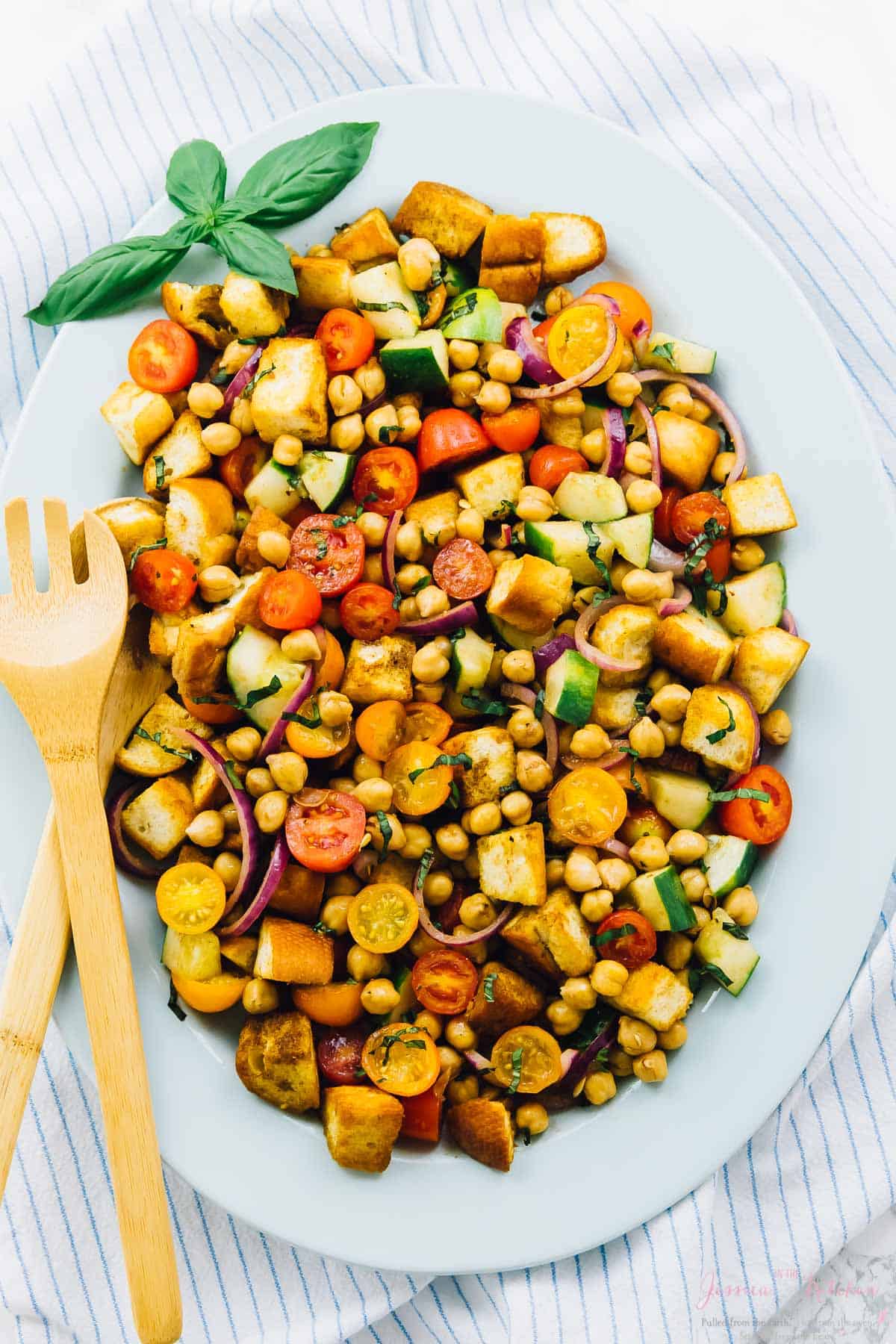 Overhead view of chickpea panzanella salad on a long white plate with a salad fork on the side. 