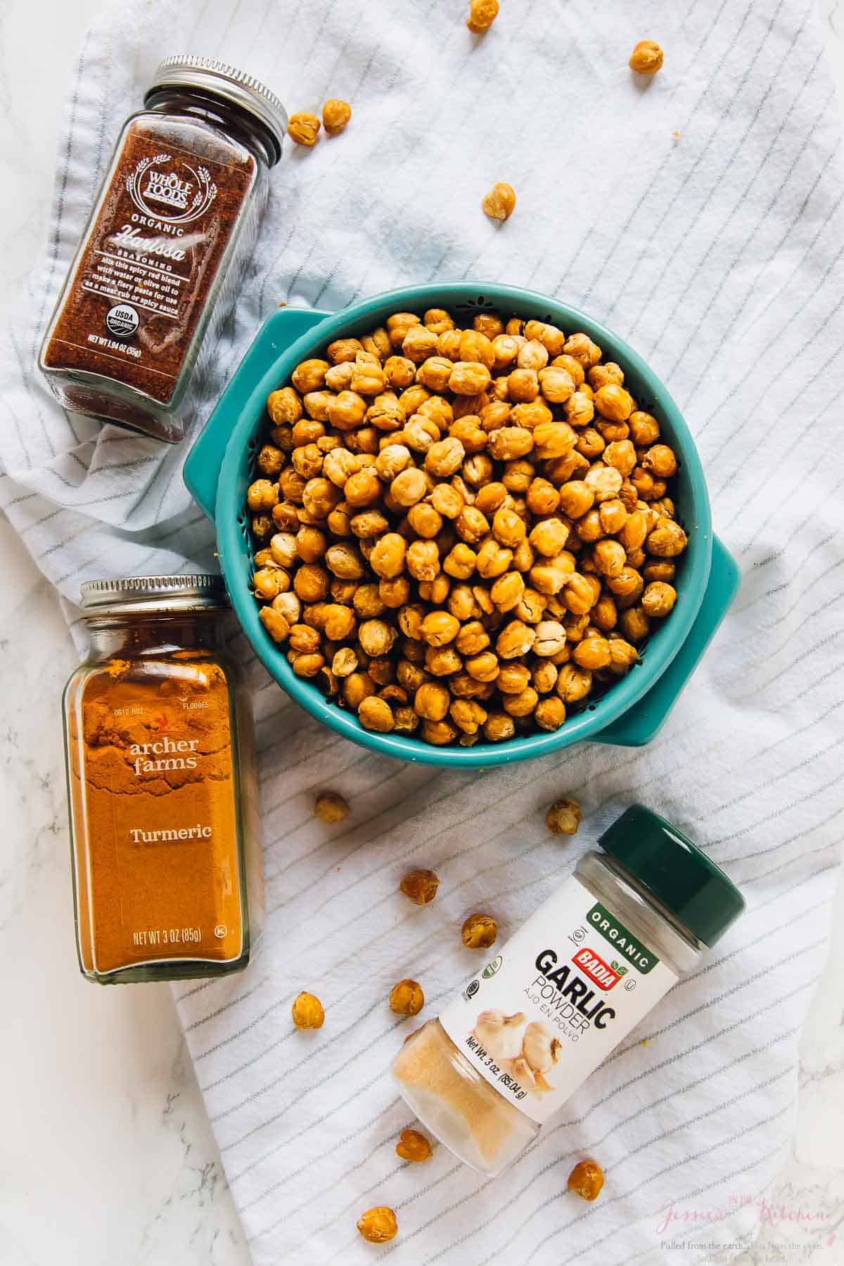 Overhead view of crispy roasted chickpeas in bowl, surrounded by spice jars