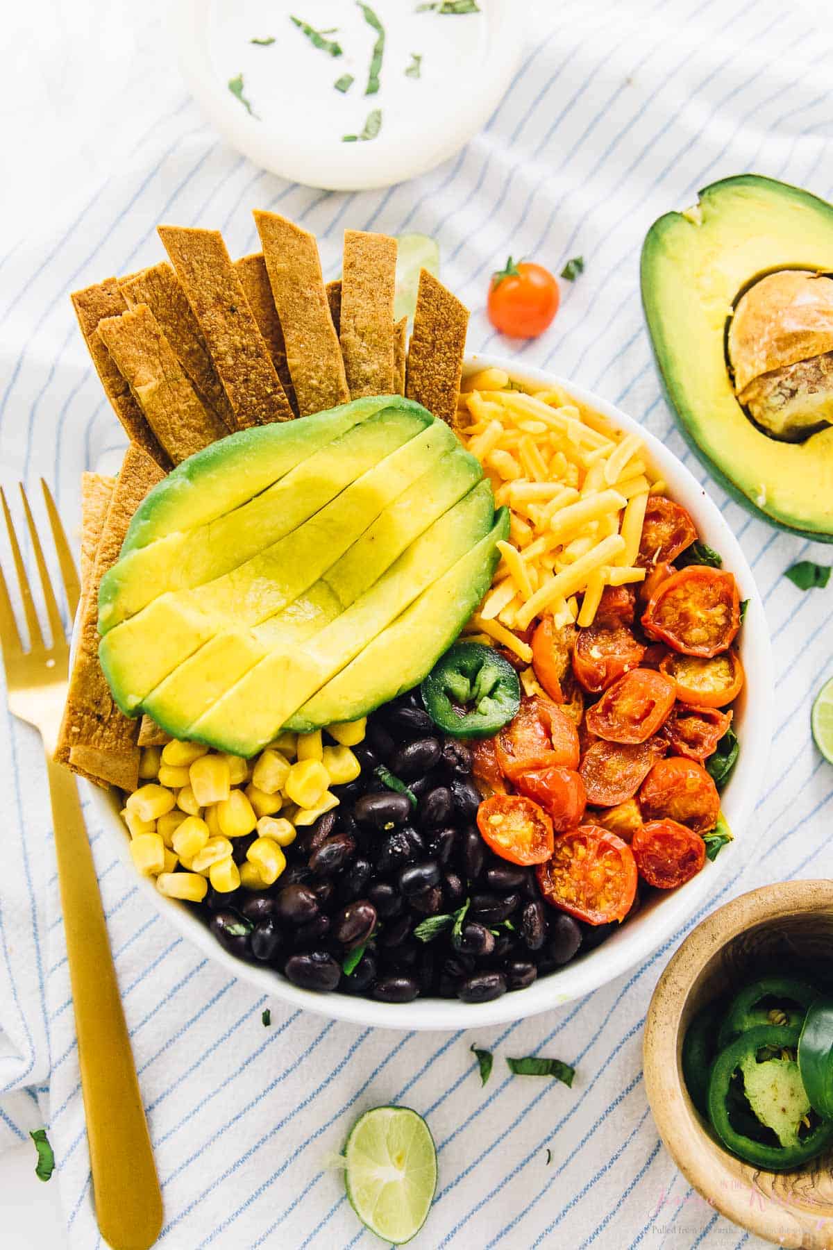 Top down shot of taco bowl on a striped cloth with a bowl of jalapenos on the side. 