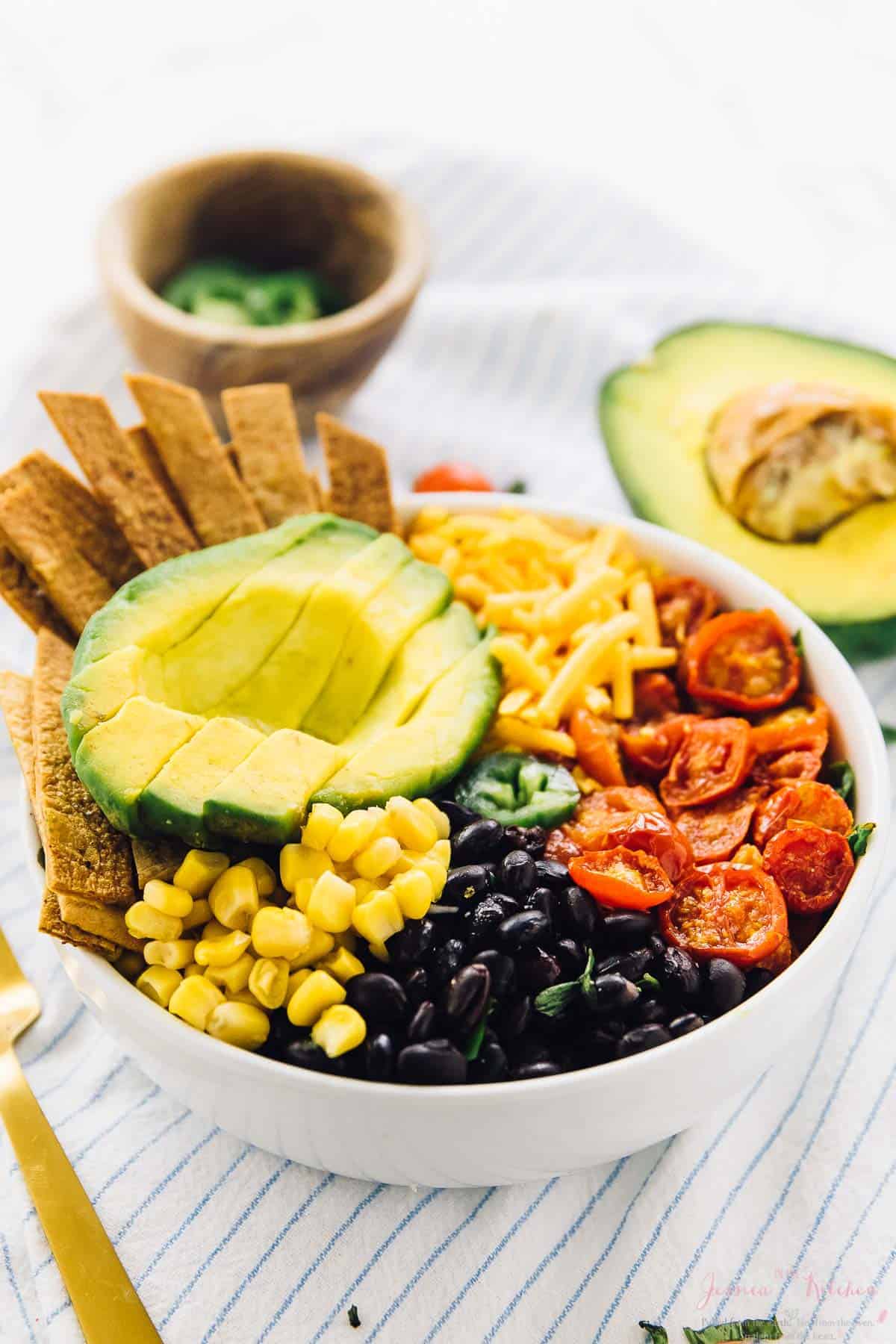 Taco salad bowl on a striped cloth with half an avocado in the background. 