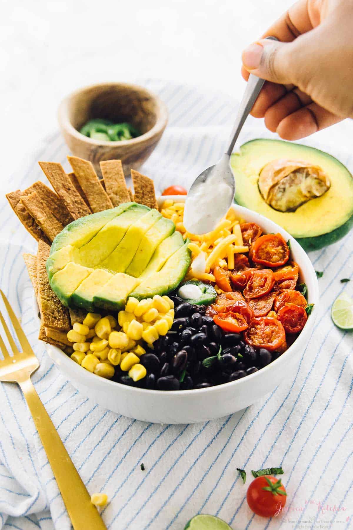 Spoon drizzling crema on a loaded taco salad bowl. 