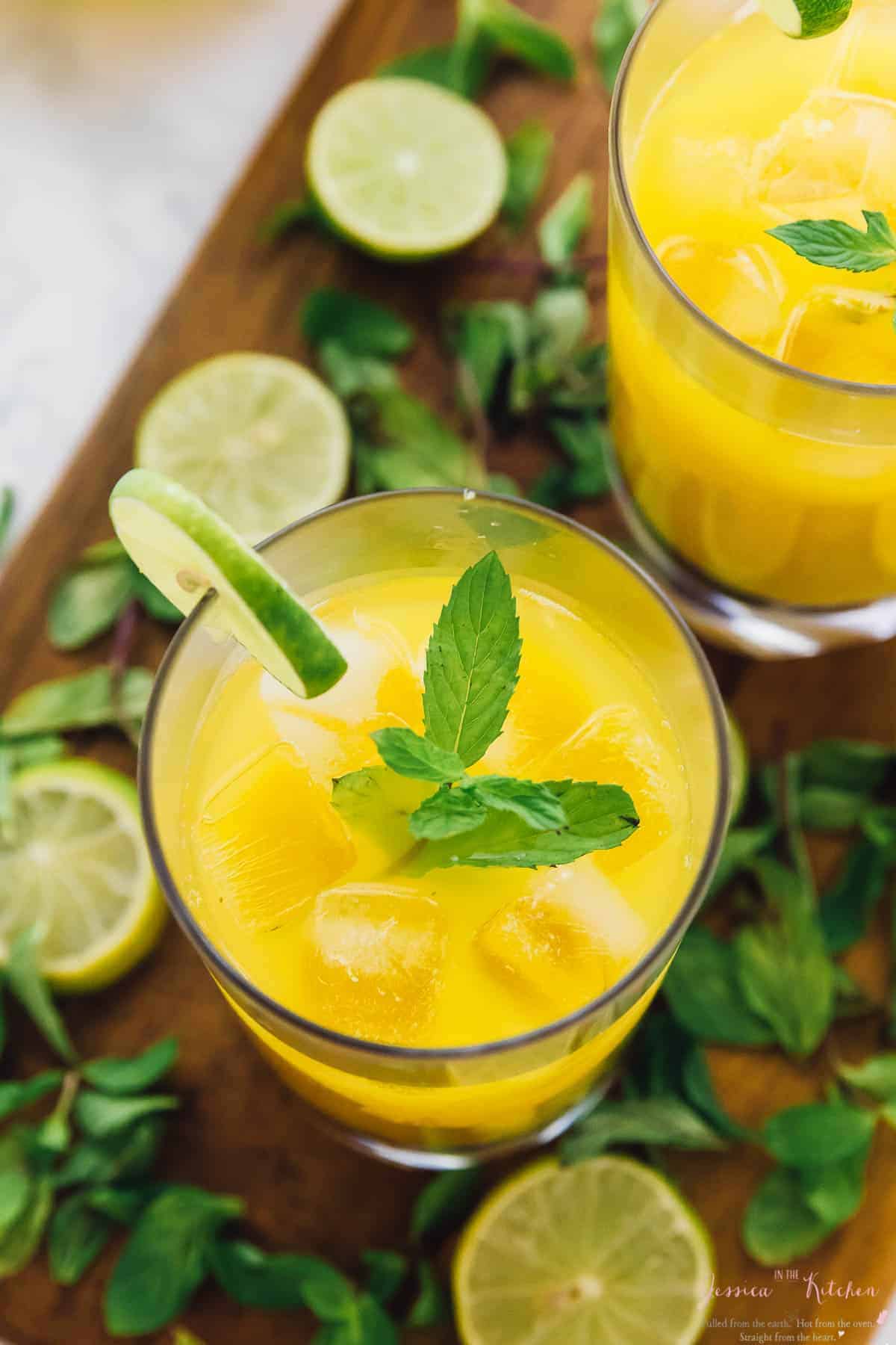 Overhead view of mango mojitos on a wooden board with slices of lime on the side. 