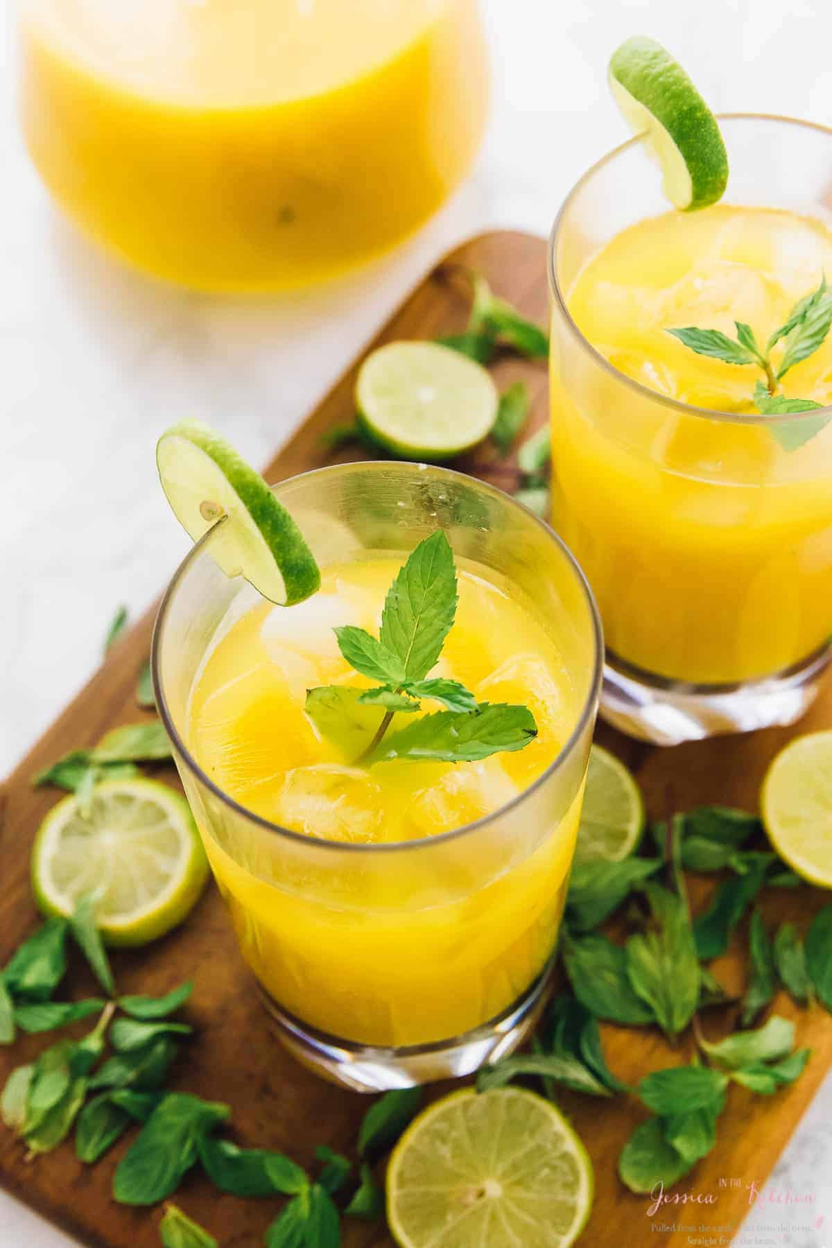 Top down view of mango mojitos on a wood board with mint and lime. 