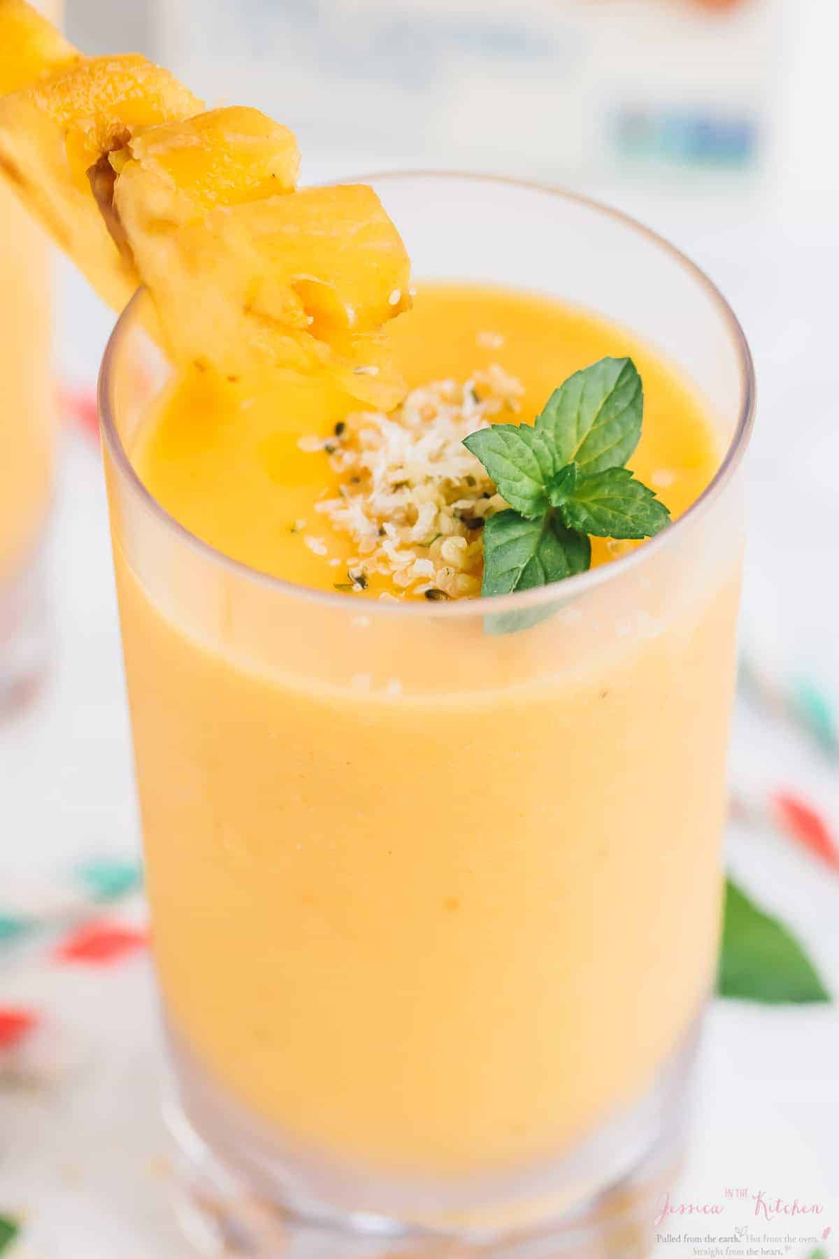 Close up of a pineapple peach smoothie in a glass, garnished with a pineapple slice. 