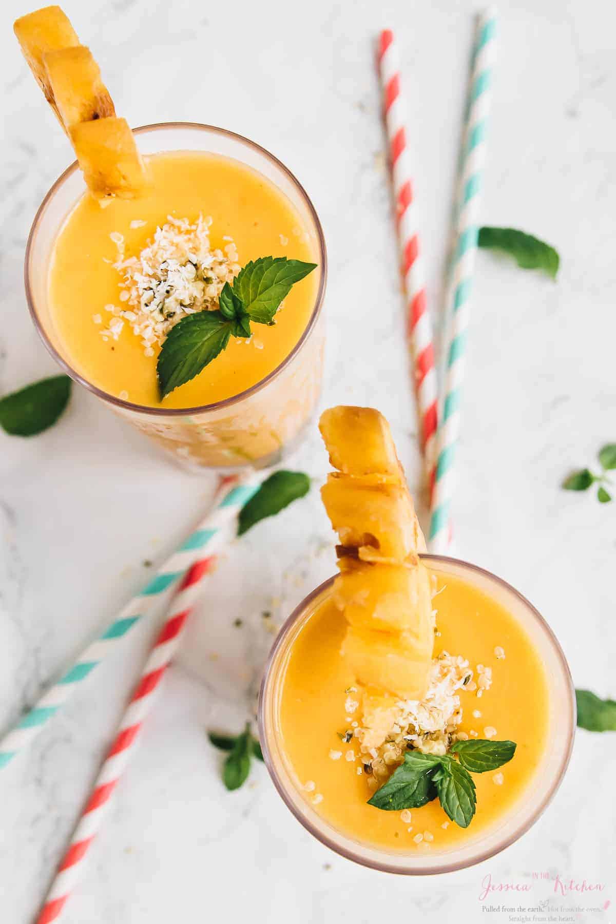 Overhead view of two pineapple peach smoothies in glasses with straws beside them. 