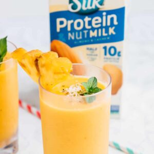 Side shot of a smoothie in a glass with a carton of nut milk in the background.