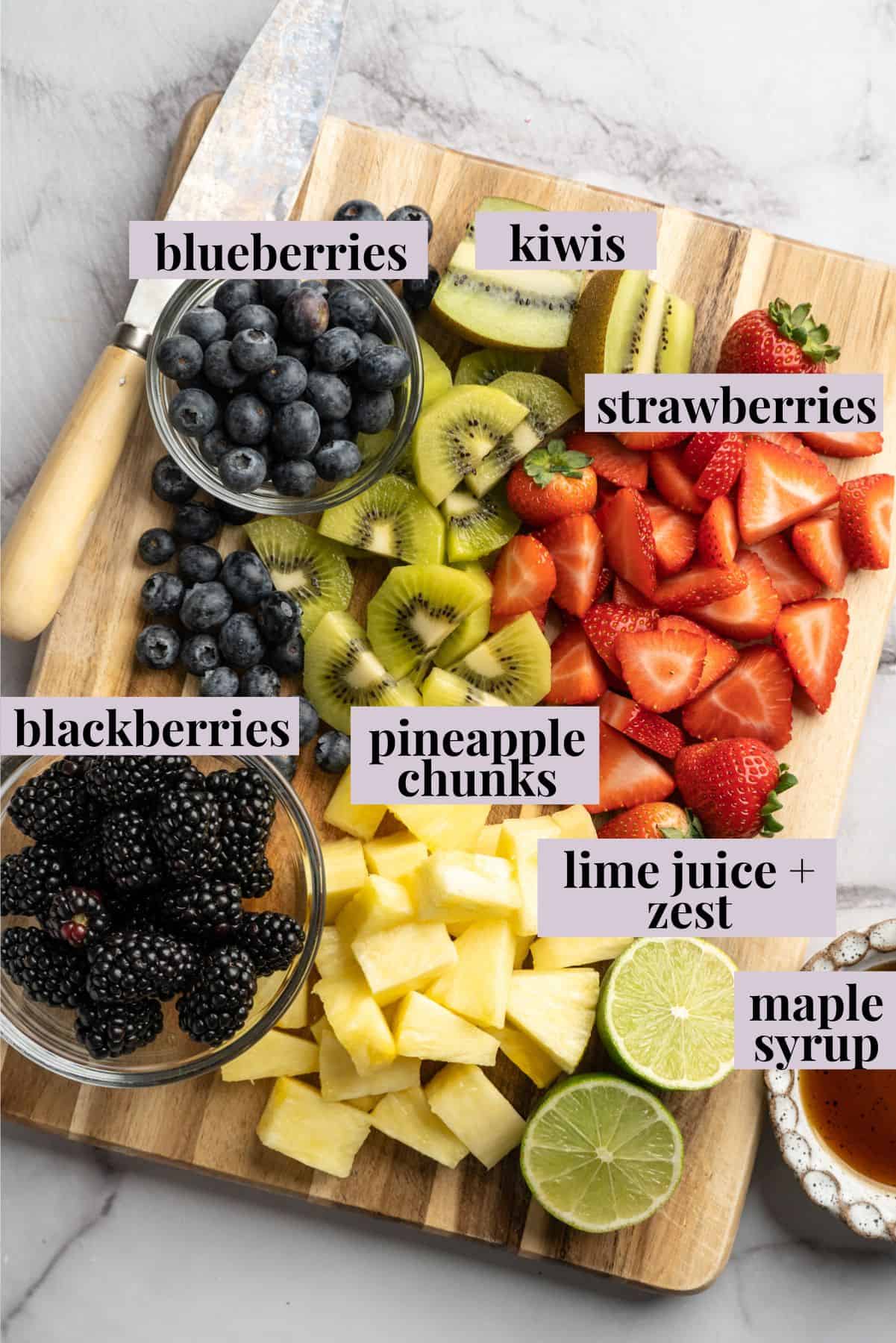 This bright rainbow fruit salad is tossed in a fresh maple lime dressing for a side that's juicy, refreshing, and perfect for any occasion! Ingredients for rainbow fruit salad on cutting board with labels.