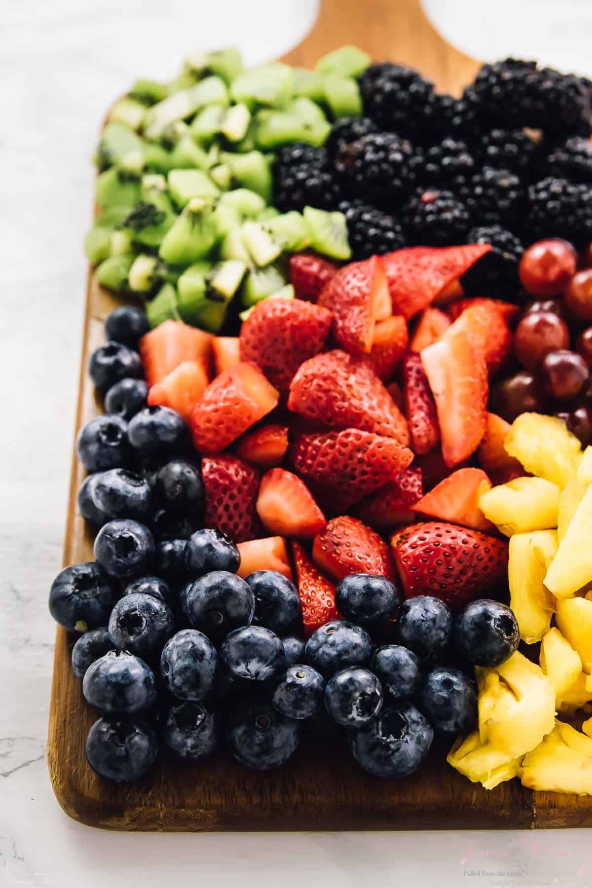 Chopped strawberries, kiwi, grapes, pineapple and blackberries on a wooden board. 