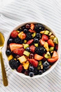 Top down view of fruit salad in a bowl with a gold spoon on the side.