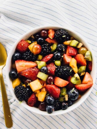 Top down view of fruit salad in a bowl with a gold spoon on the side.