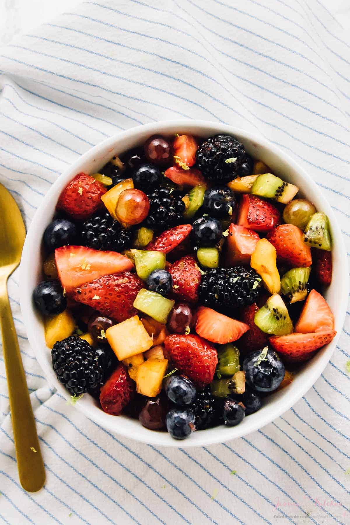 Overhead view of rainbow fruit salad in a bowl on a striped cloth. 