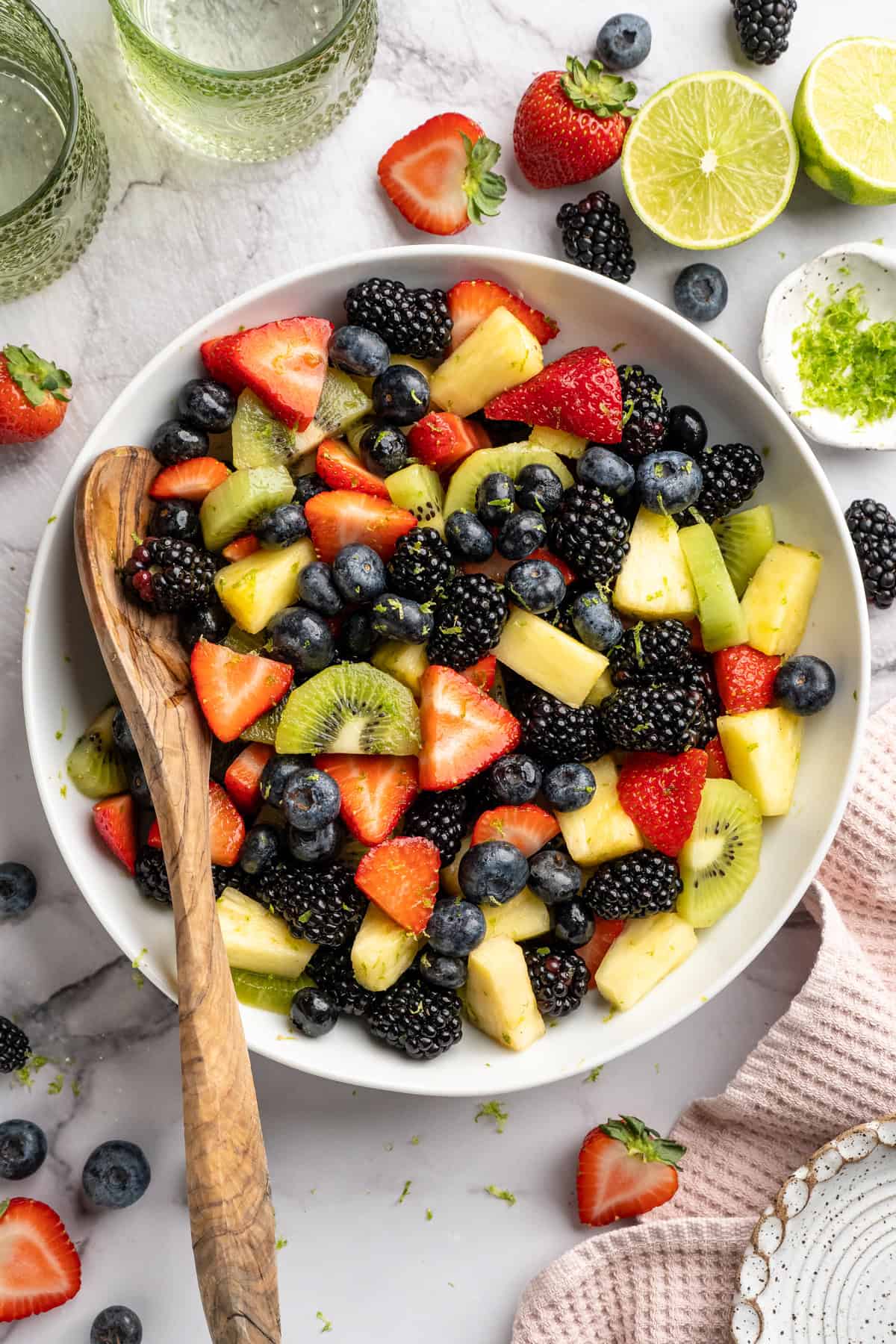 This bright rainbow fruit salad is tossed in a fresh maple lime dressing for a side that's juicy, refreshing, and perfect for any occasion! Serving bowl of rainbow fruit salad with berries, kiwi, and pineapple.