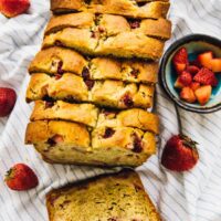 Overhead view of sliced strawberry banana bread on a cloth with a bowl of diced strawberries on the side.