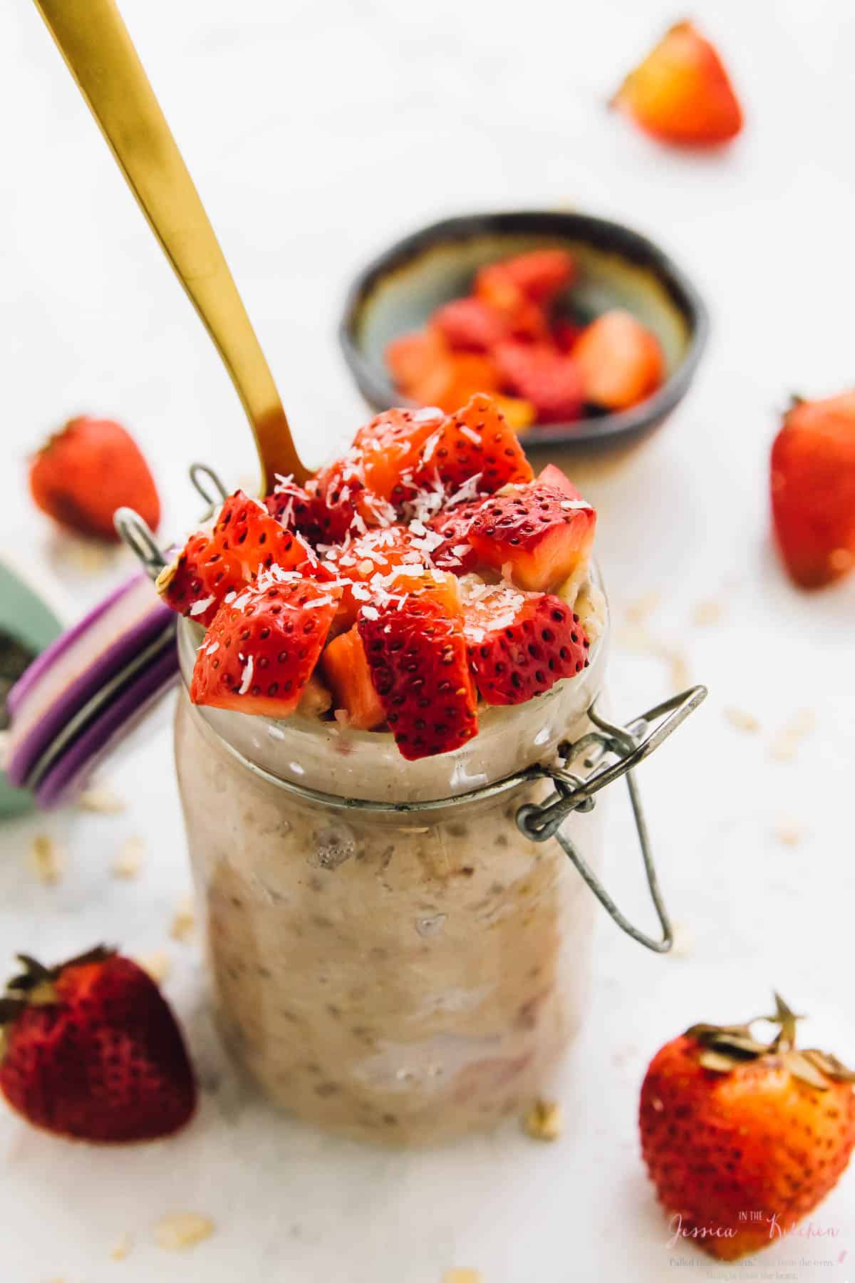 Spoon dipping into strawberry Coconut overnight oats in a small glass jar with diced strawberries on top. 