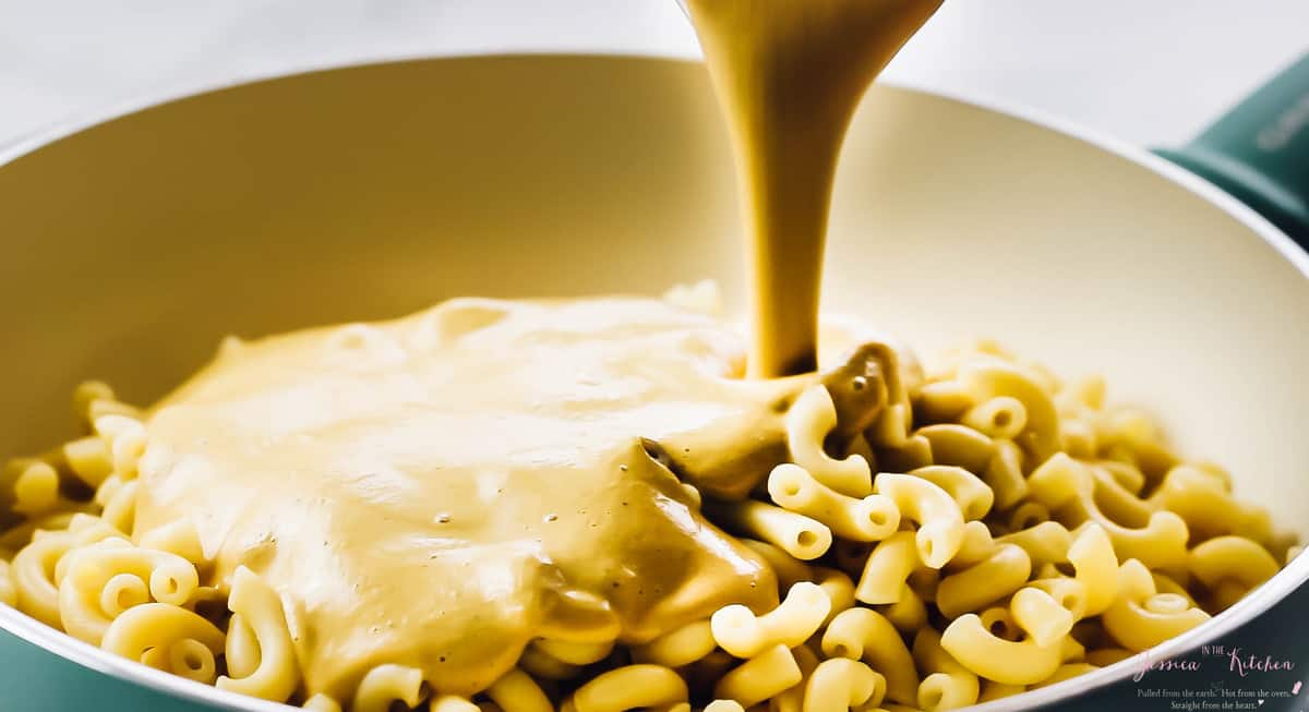 Pouring cheese sauce on macaroni in a skillet. 