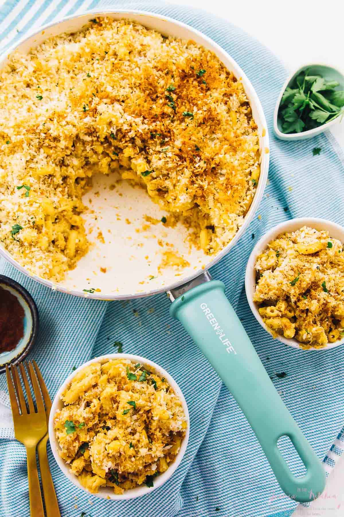 Overhead shot of creamy baked vegan mac and cheese in a skillet and two bowls.