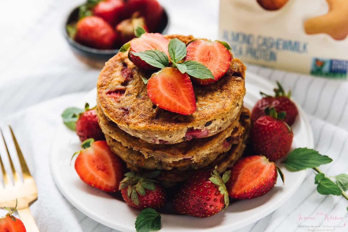 A pile of gluten free strawberry pancakes surrounded by strawberries. 