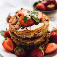 Drizzling syrup onto stack of vegan gluten-free strawberry pancakes