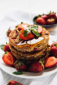 A pile of fluffy vegan strawberry pancakes drizzled with syrup.