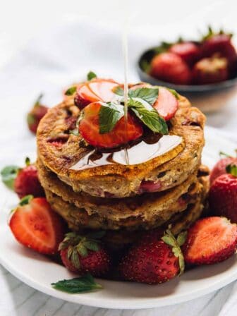 Drizzling syrup onto stack of vegan gluten-free strawberry pancakes