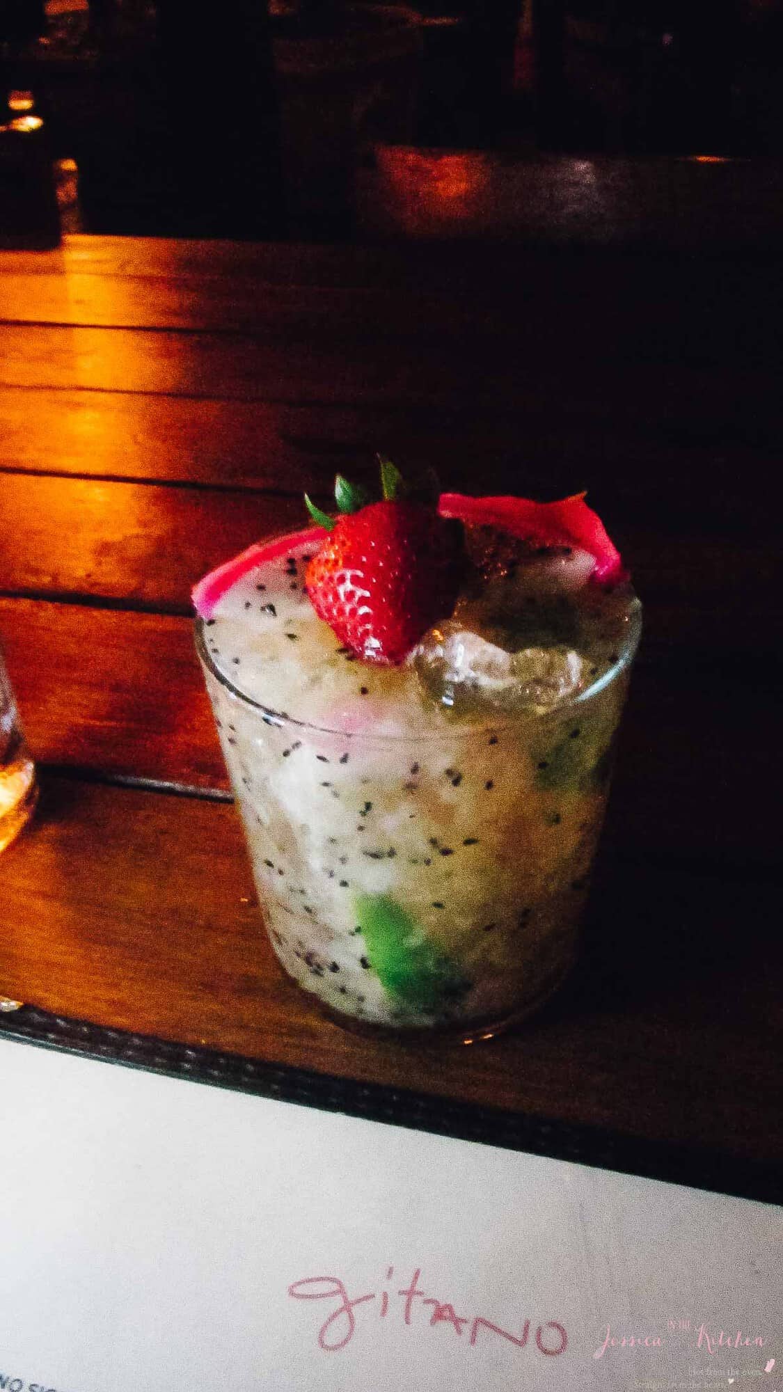 A white cocktail with a strawberry garnish on a wood table. 