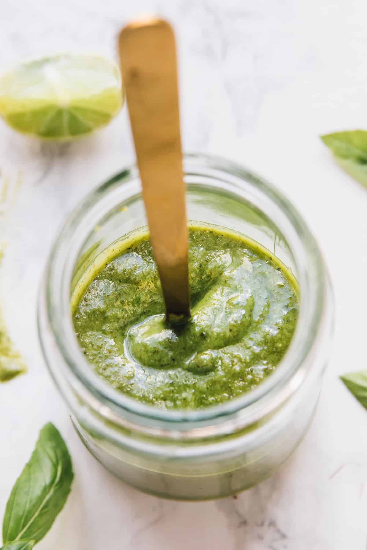 Overhead view of basil pesto in a glass jar with a gold spoon. 