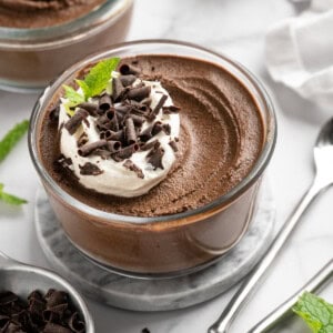 Bowl of chocolate avocado pudding with coconut whipped cream and chocolate shavings on top.