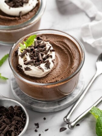 Bowl of chocolate avocado pudding with coconut whipped cream and chocolate shavings on top.