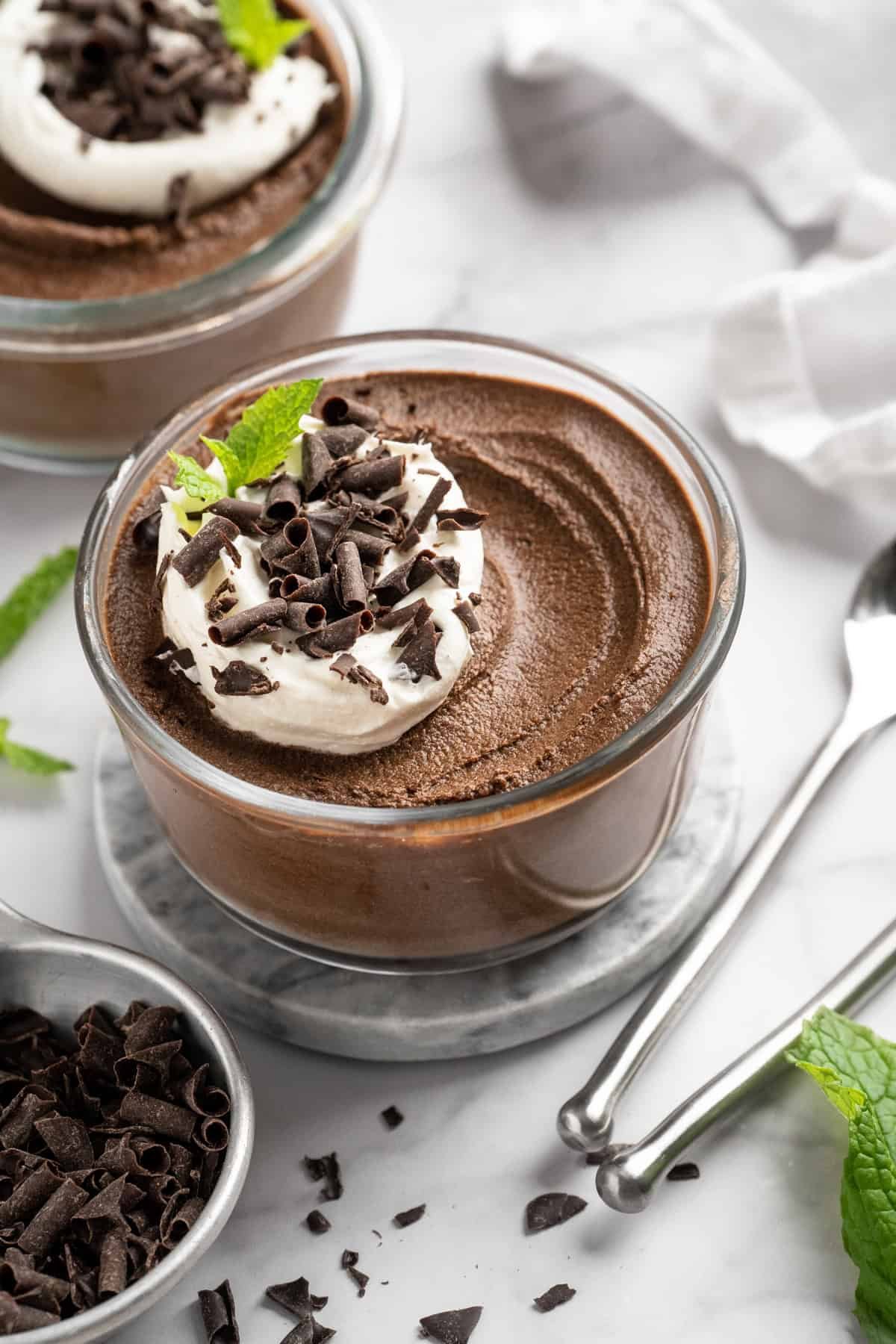 Bowl of chocolate avocado pudding with coconut whipped cream and chocolate shavings on top.