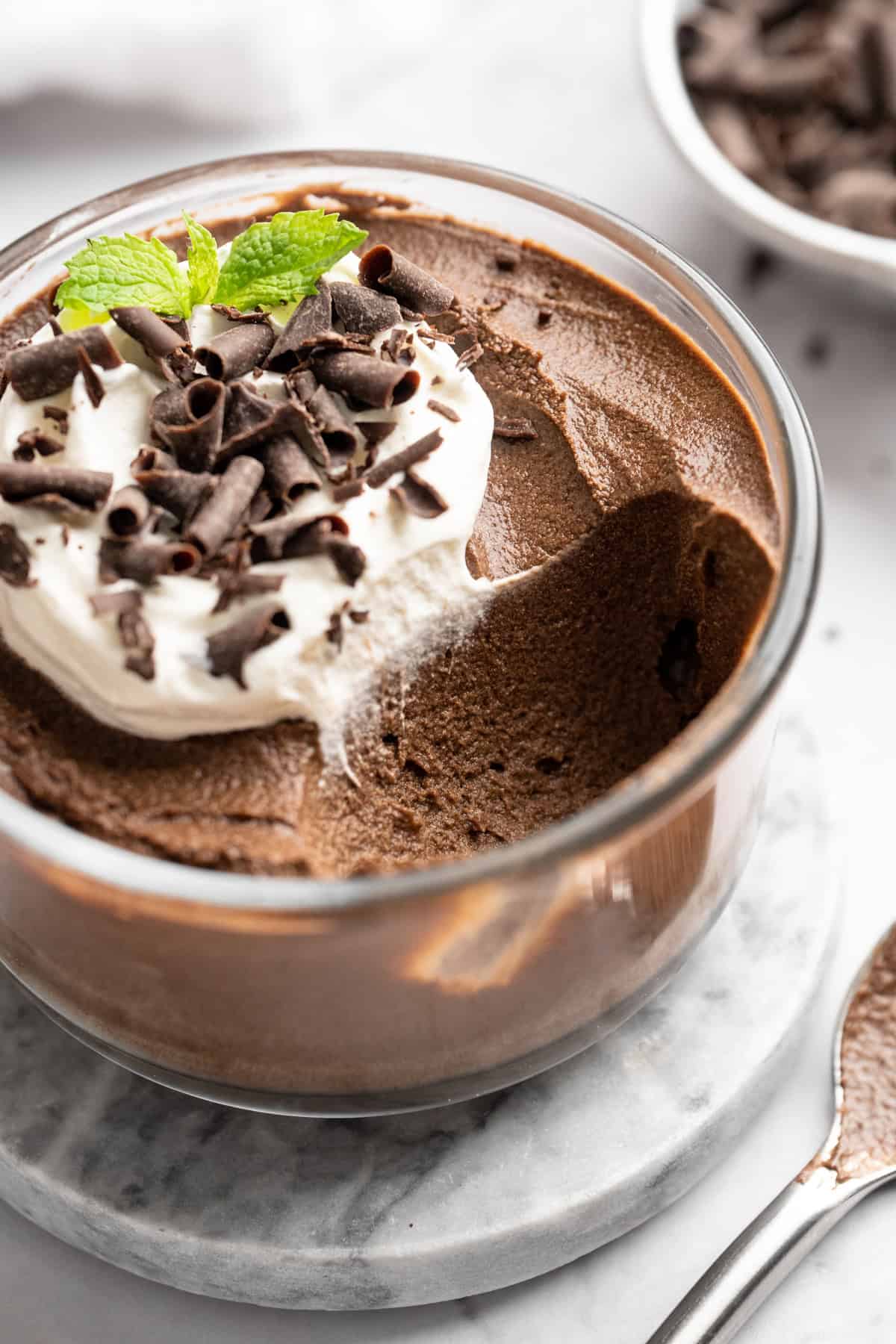 Chocolate avocado pudding in glass bowl topped with coconut whipped cream and chocolate shavings