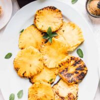 Overhead view of grilled pineapple slices with mint garnish.