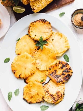 Overhead view of grilled pineapple slices with mint garnish.