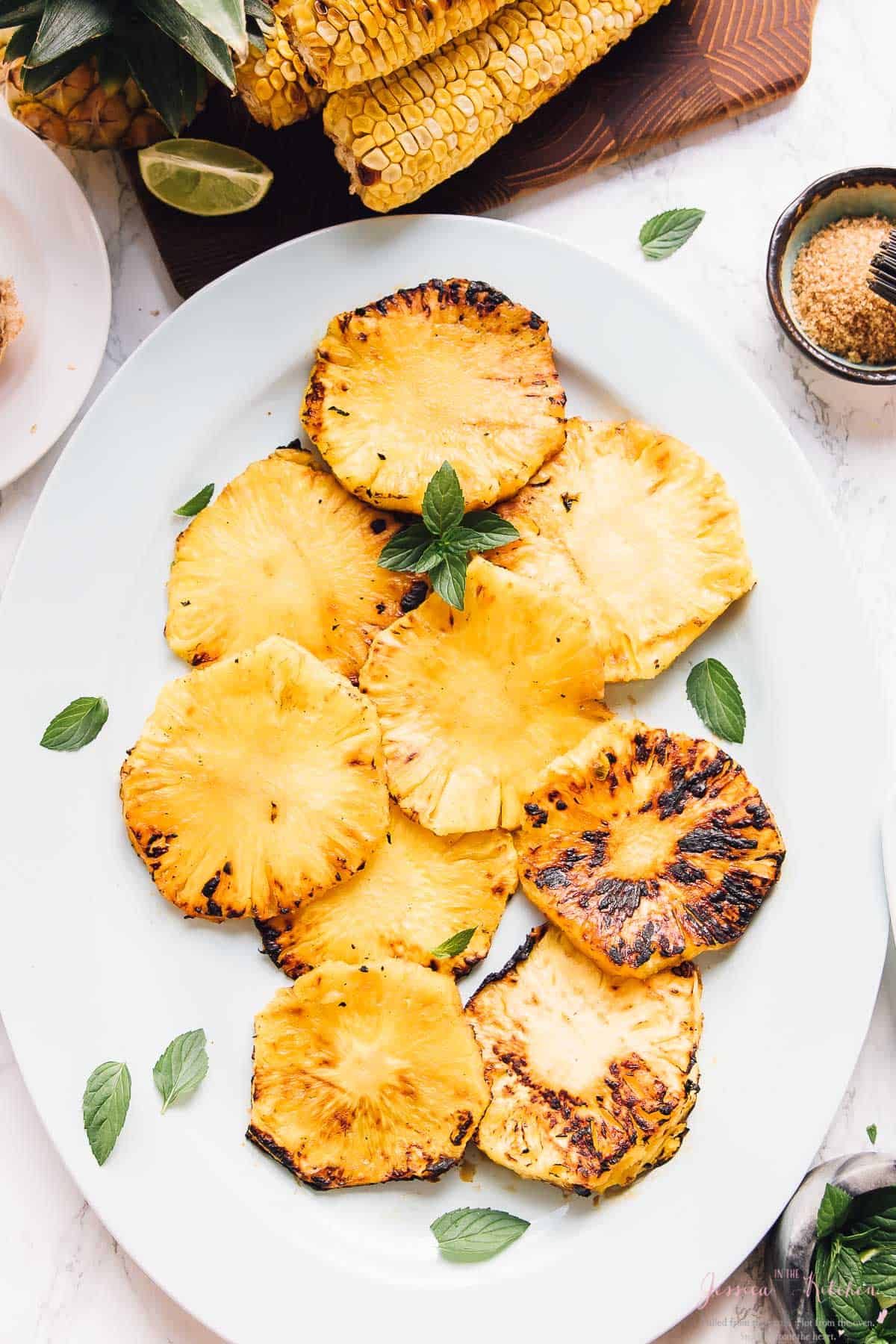 Overhead view of grilled pineapple slices on a long white dish. 
