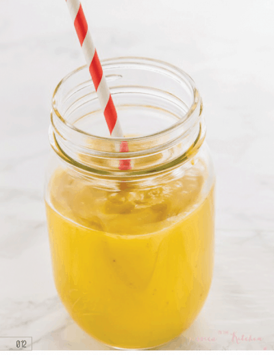 Mango turmeric smoothie in a glass mason jar with a red straw.