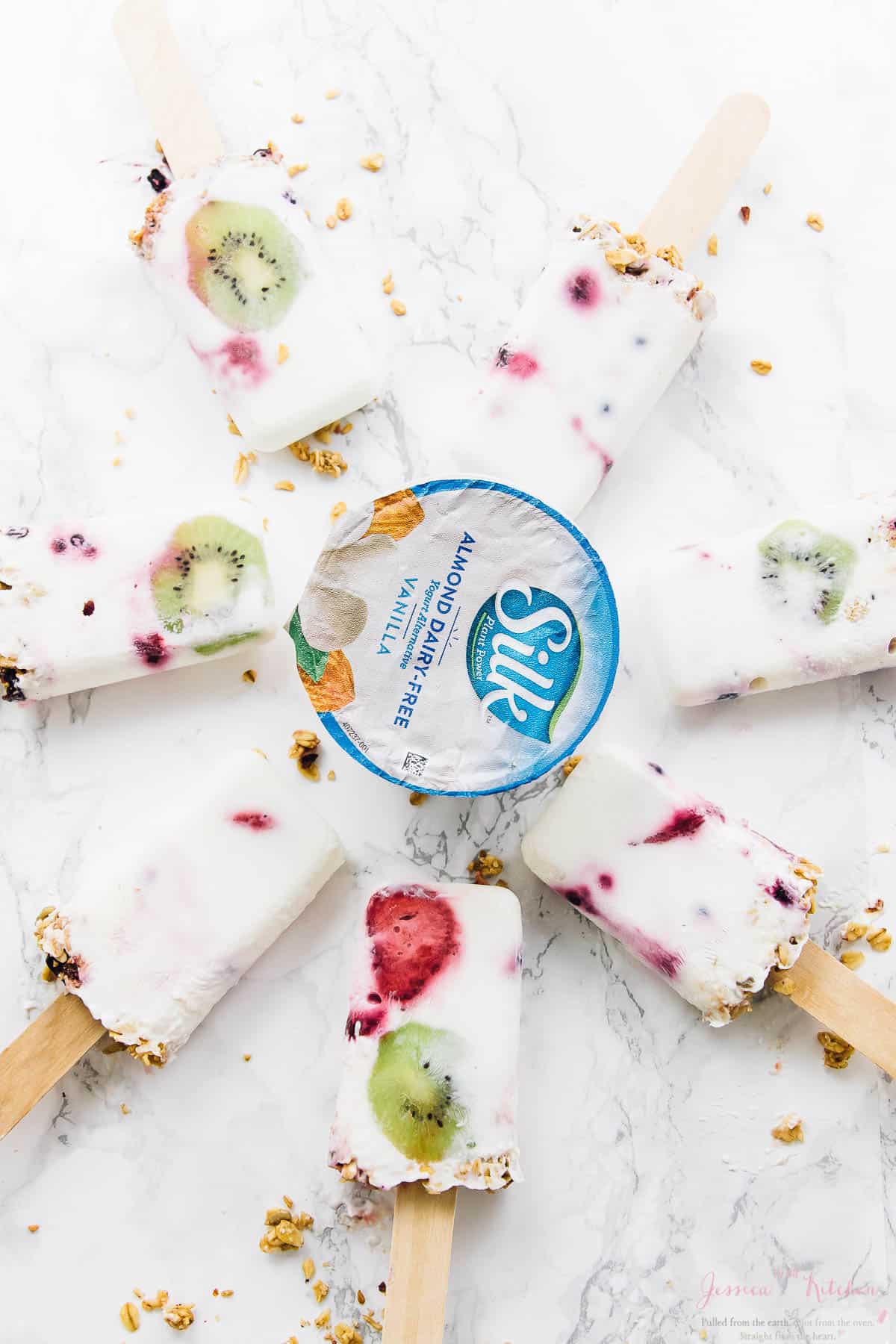 Top down shot of vegan yogurt parfait breakfast popsicles around a pot of dairy free yogurt. 