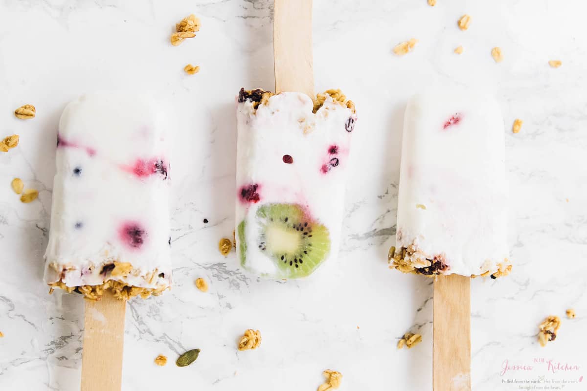 Top down view of three vegan yogurt parfait breakfast popsicles on a white table. 