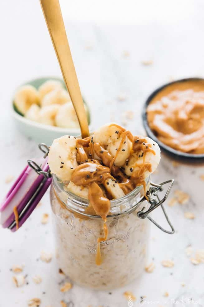 Overnight oats in a glass jar with peanut butter drizzled over it and the banana.
