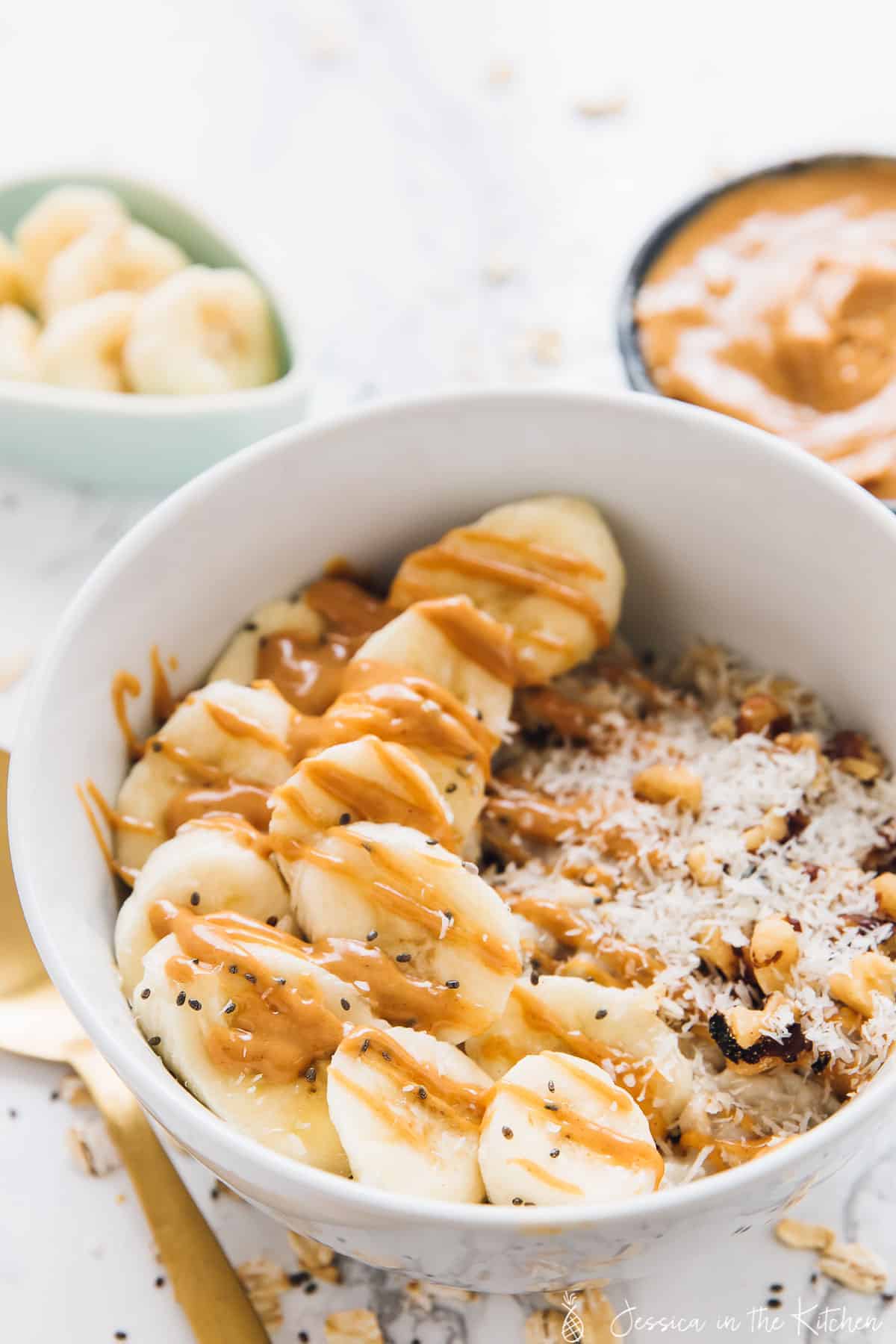 Oats in a white bowl with slices bananas and peanut butter drizzled on top.