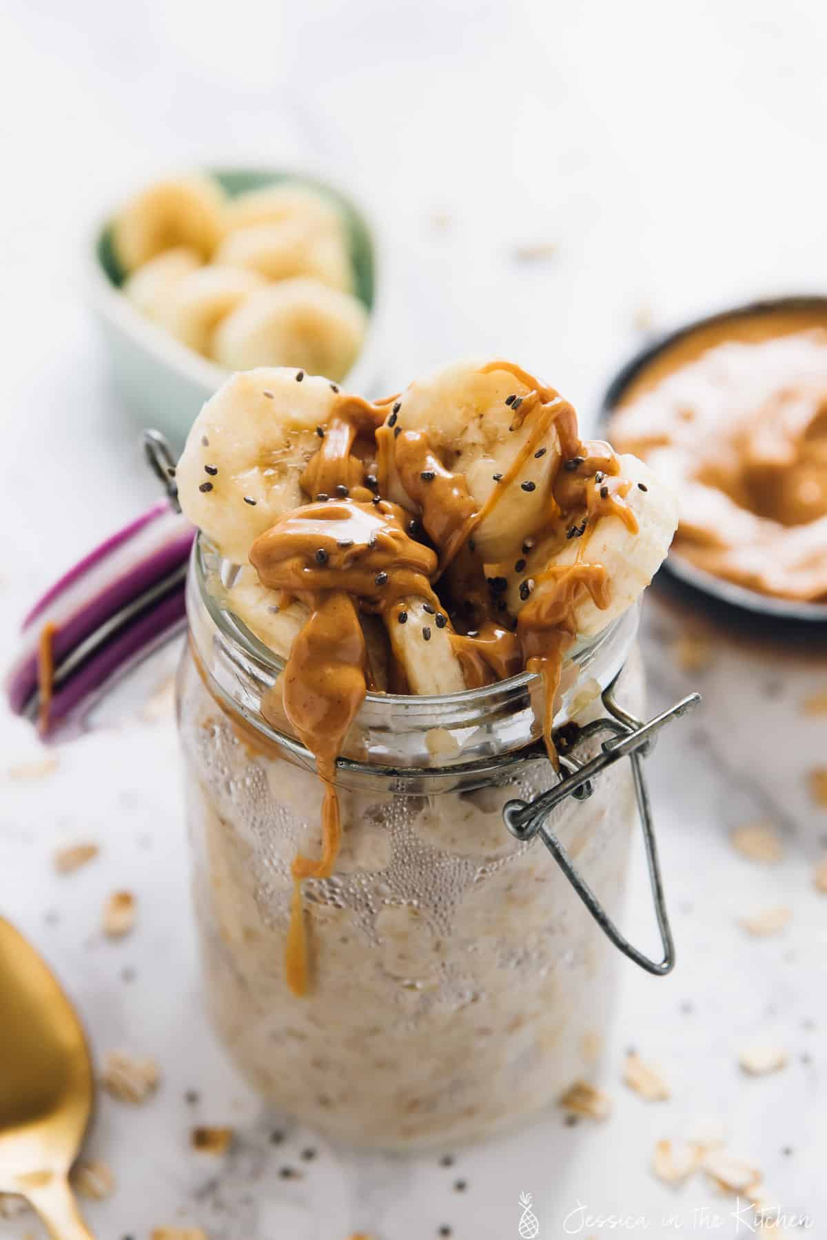 A jar of peanut butter banana overnight oats with sliced bananas in the background. 