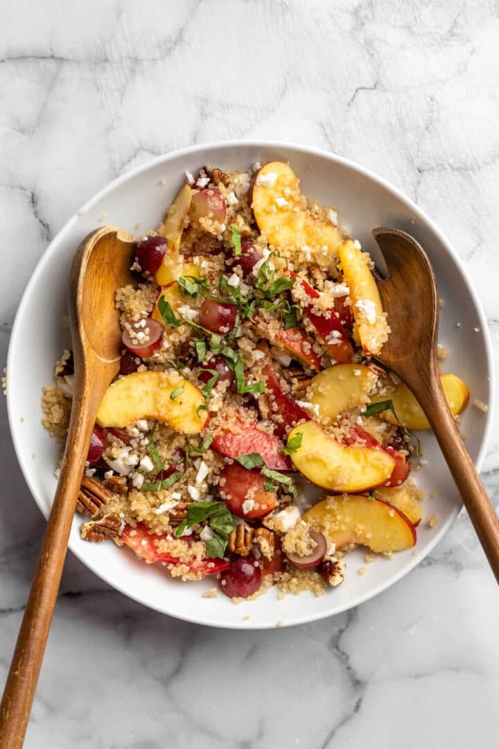 Sweet, juicy summer fruit and fluffy quinoa come together in this beautiful quinoa stone fruit salad. It’s ready in just 20 minutes! Two wooden spoons in bowl of quinoa stone fruit salad.