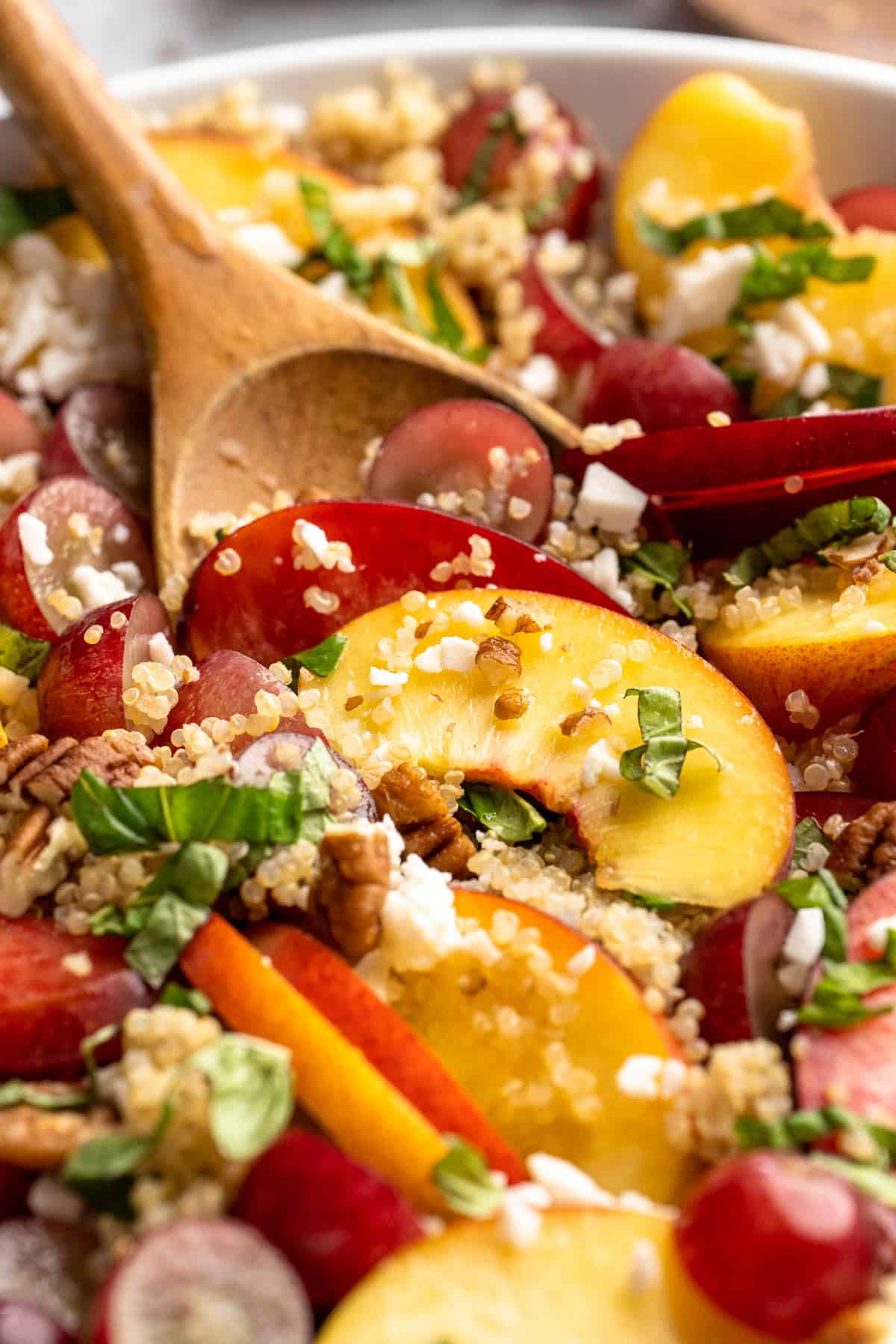 Sweet, juicy summer fruit and fluffy quinoa come together in this beautiful quinoa stone fruit salad. It’s ready in just 20 minutes! Stirring quinoa stone fruit salad with wooden spoon.