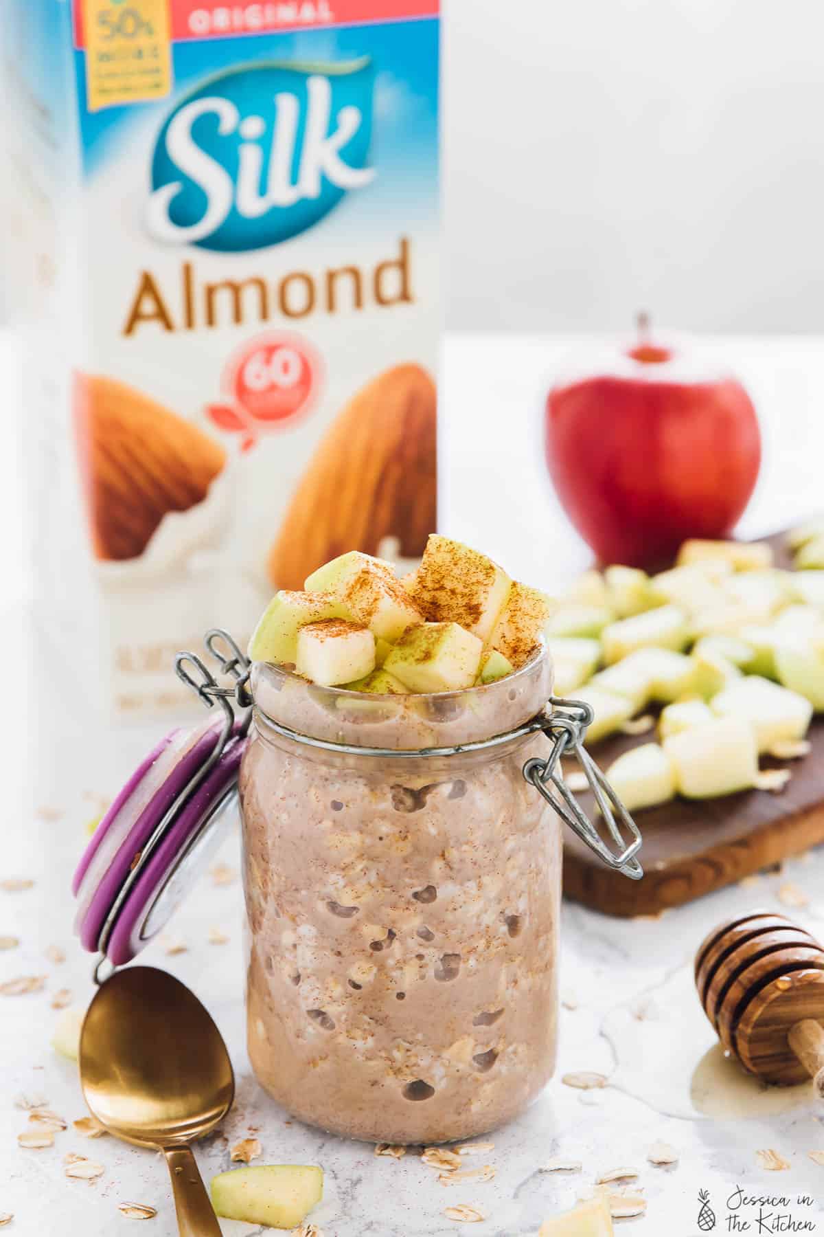 Apple cinnamon overnight oats in a jar with a carton of almond milk in the background. 