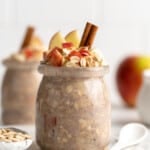 two jars apple overnight oats with cinnamon sticks, oats and apples topping them