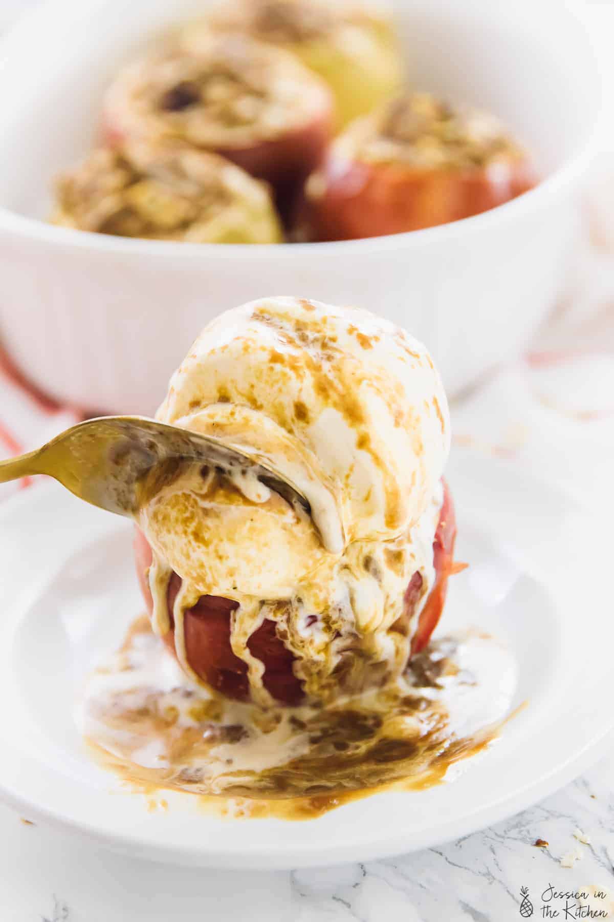 Spoon cutting into a baked apple and ice cream. 