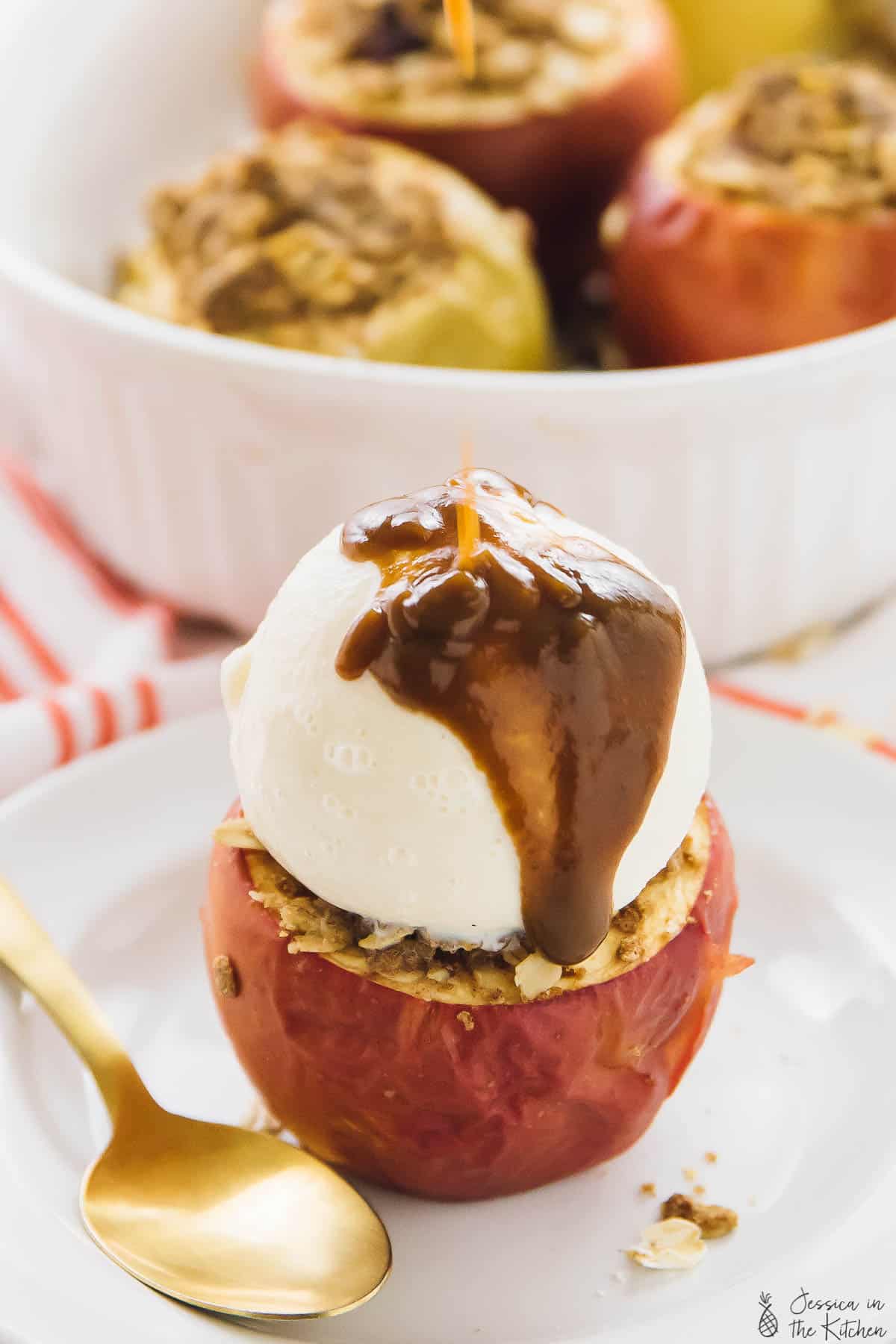 A baked apple topped with ice cream and a gold spoon on the side. 