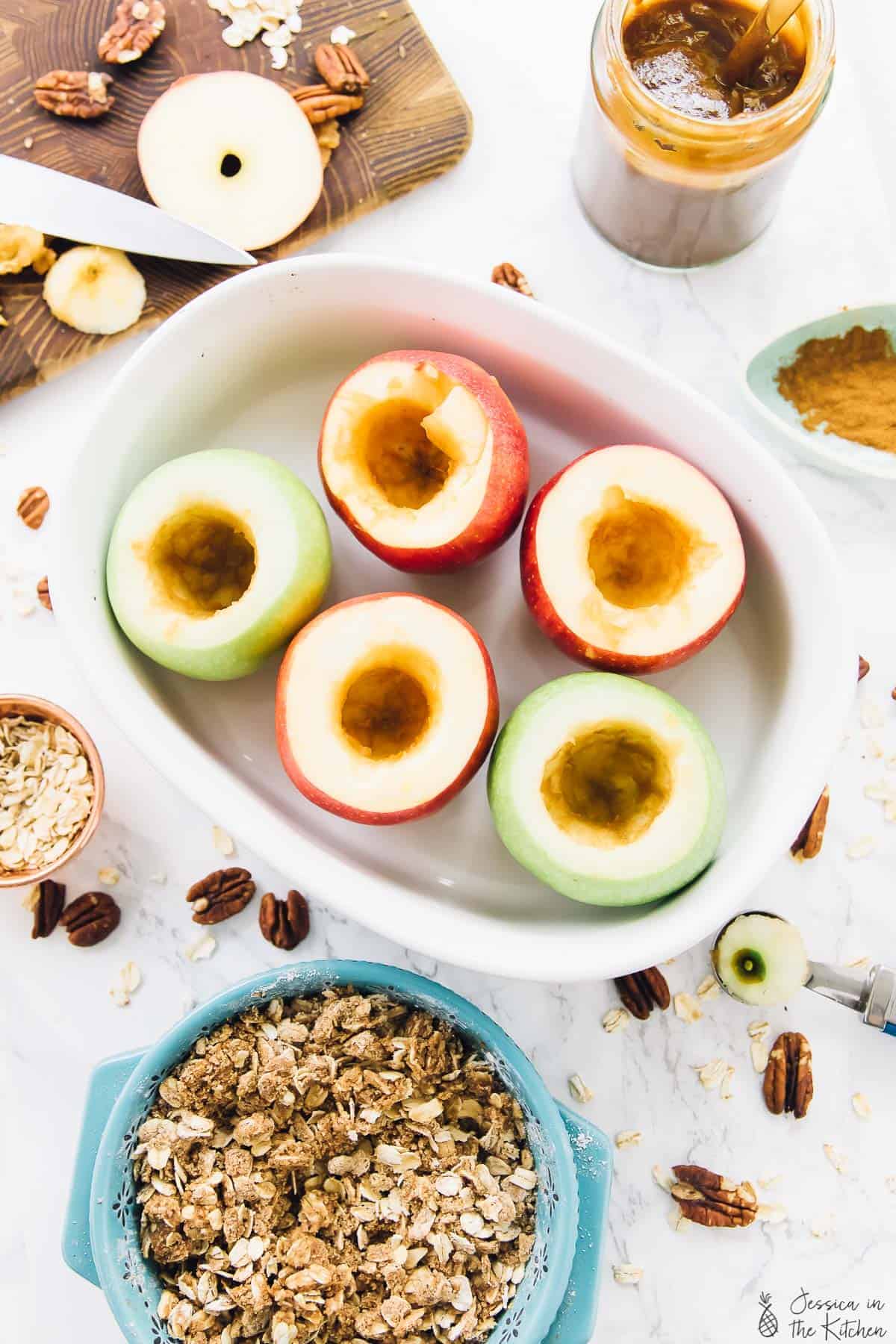 Top down view of cored apples in a baking dish with a bowl of oats next to it. 