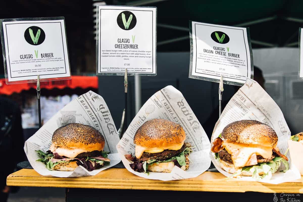 Three burgers on a wood plank.